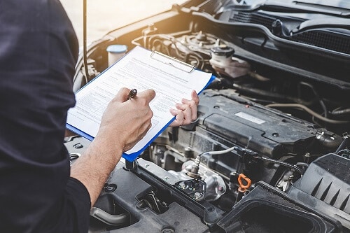 Factory Scheduled Maintenance | EG Auto Center in Dayton, NJ. Image of an auto mechanic checking a car engine with clipboard of the checklist for car repair, service, and maintenance.