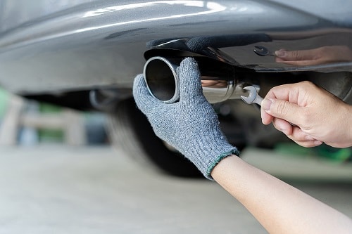 Exhaust System Repair | EG Auto Center in Dayton, NJ. Closeup image of a mechanic's hand fixing a car exhaust and using open-end wrench for service in concept maintenance car in garage.