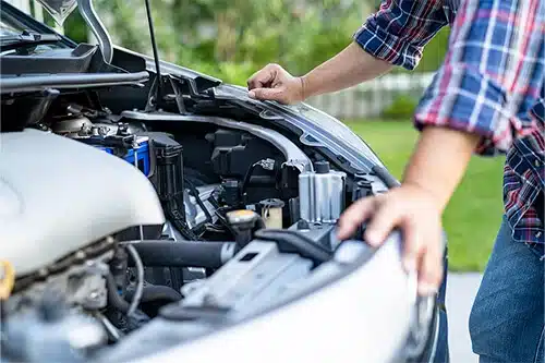 Prepare You Car for the Cold With These Simple Fall Car Care Tips | EG Auto Center in Dayton, NJ. Image of a car owner looking under the hood of a car to check engine, battery, and other components.