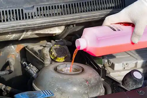 Chill Out! Don't Forget These Pre-Winter Cooling System Services | EG Auto Center in Dayton, NJ. Image of a mechanic’s hand pouring pink coolant into an engine reservoir.