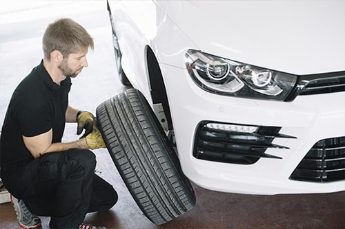 An auto mechanic changing the tire of a white car. Concept image for “5 Spring Car Care Tips Every Car Owner Should Know” | EG Auto Center in Dayton, NJ.